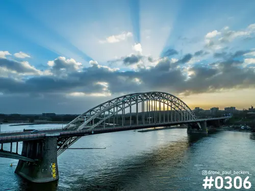 Luchtfoto van de Waalbrug in Nijmegen met zonnestralen die door donkere wolken breken boven de rivier de Waal