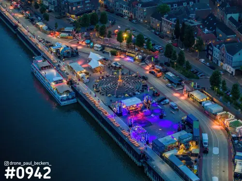 Luchtfoto van de Waalkade in Nijmegen in de avond, met verlicht evenemententerrein en een cruiseschip aan de Waal
