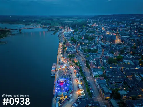 Luchtfoto van de Waalkade in Nijmegen in het blauwe uur, met verlichte tenten, de Waalbrug en de rivier de Waal