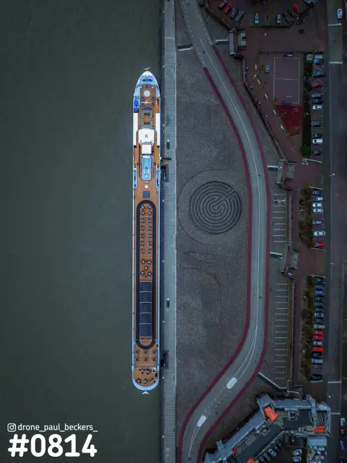 Luchtfoto van een riviercruiseschip aan de Waalkade in Nijmegen, recht van boven, naast een rond labyrint in de bestrating