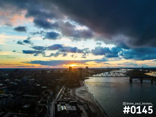 Luchtfoto van de Waalkade in Nijmegen bij zonsondergang, met de Oversteek over de Waal en een donkere wolkenlucht