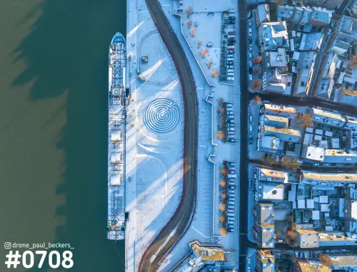 Luchtfoto van de besneeuwde Waalkade in Nijmegen met een afgemeerd schip en een cirkelvormig patroon op het plein