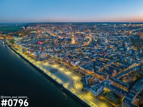 Luchtfoto van de Waalkade in Nijmegen in de blauwe avondschemering, met verlichte kade langs de Waal en de Stevenskerk