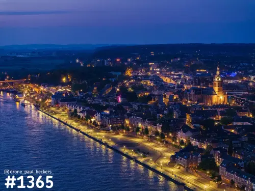 Luchtfoto van de Waalkade en Stevenskerk in Nijmegen in het blauwe uur, met verlichte kade langs de rivier de Waal
