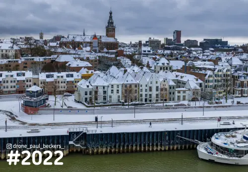 Luchtfoto van de besneeuwde Waalkade in Nijmegen, met de Stevenskerk boven de daken en een schip aan de kade