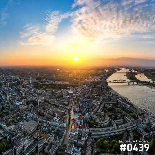 Luchtfoto van Nijmegen met de Waal en de Waalkade bij zonsondergang, met een boogbrug over de rivier en sluierwolken