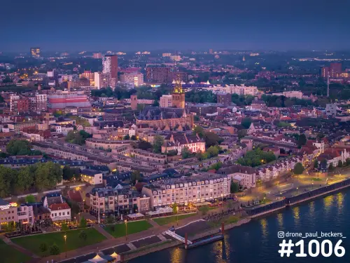 Luchtfoto van de Waalkade en Stevenskerk in Nijmegen in de avondschemering, met verlichte gevels en reflecties op de Waal
