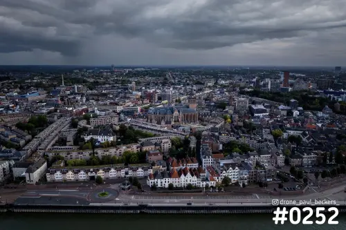 Luchtfoto van Nijmegen vanaf de Waal met de Waalkade en de Stevenskerk onder een donkere, dreigende wolkenlucht