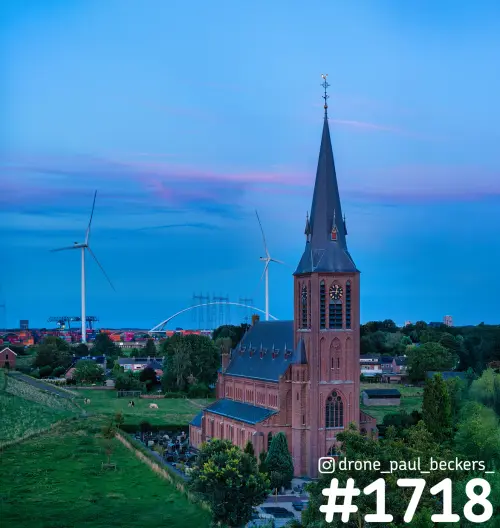 Luchtfoto van de rode baksteenkerk in Weurt bij Nijmegen in het blauwe uur, met De Oversteek en windmolens op de achtergrond