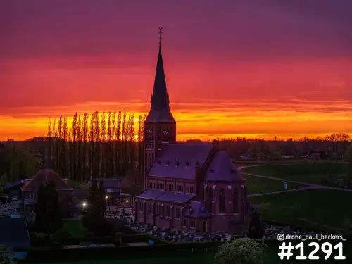 Luchtfoto van de bakstenen kerk in Weurt bij zonsondergang, met populieren als silhouet tegen een rood-oranje lucht