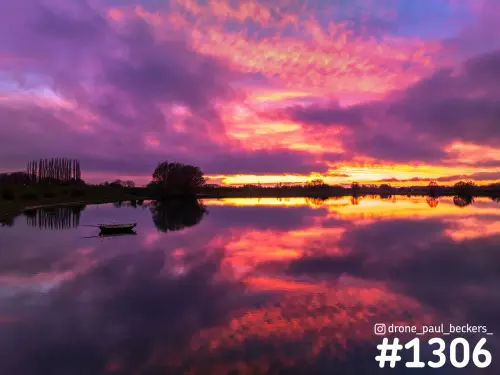 Kleurrijke lucht in paars, roze en oranje boven stil water bij Weurt, met een roeiboot en bomen die weerspiegelen