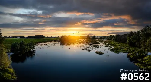 Luchtfoto van een natuurgebied bij Weurt met een stille waterplas bij zonsondergang, onder een wolkenlucht met oranje gloed