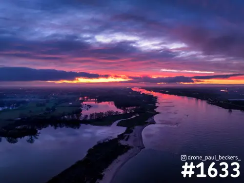 Luchtfoto van de rivier bij Weurt in de schemering, met roze en paarse wolken boven een zandbank en een stille plas