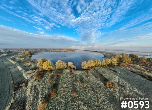 Luchtfoto van de uiterwaarden bij Weurt met een plas, berijpt gras, geel herfstloof en een hemel vol schapenwolken