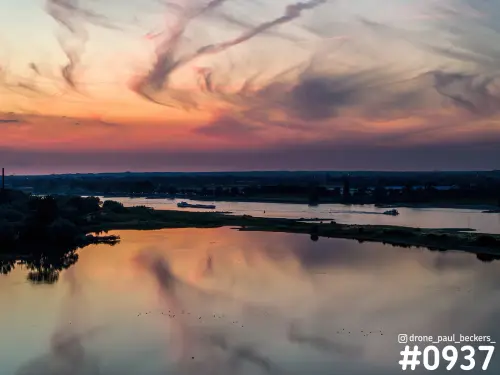 Luchtfoto van de Waal bij Weurt na zonsondergang, met roze en oranje wolkenslierten die weerspiegelen in het stille water
