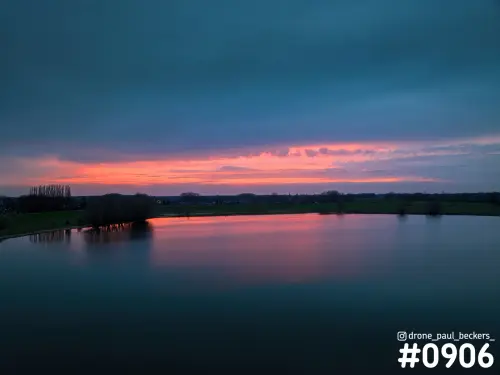 Luchtfoto van water bij Weurt na zonsondergang, met een roze en oranje gloed die weerspiegelt in het stille water