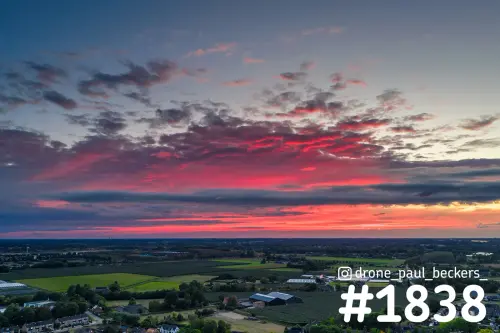 Luchtfoto van Weurt bij zonsondergang, met een felrode en paarse wolkenlucht boven groene weilanden en boomgaarden