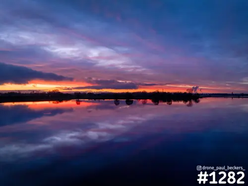 Zonsondergang bij Weurt met paarsroze wolkenlucht die weerspiegelt in het stille water, met bomen langs de horizon