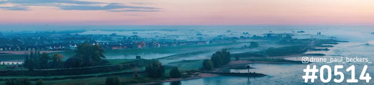 Panorama-luchtfoto van de Waal bij Lent in Nijmegen bij zonsopkomst, met mist boven de uiterwaarden en roze lucht