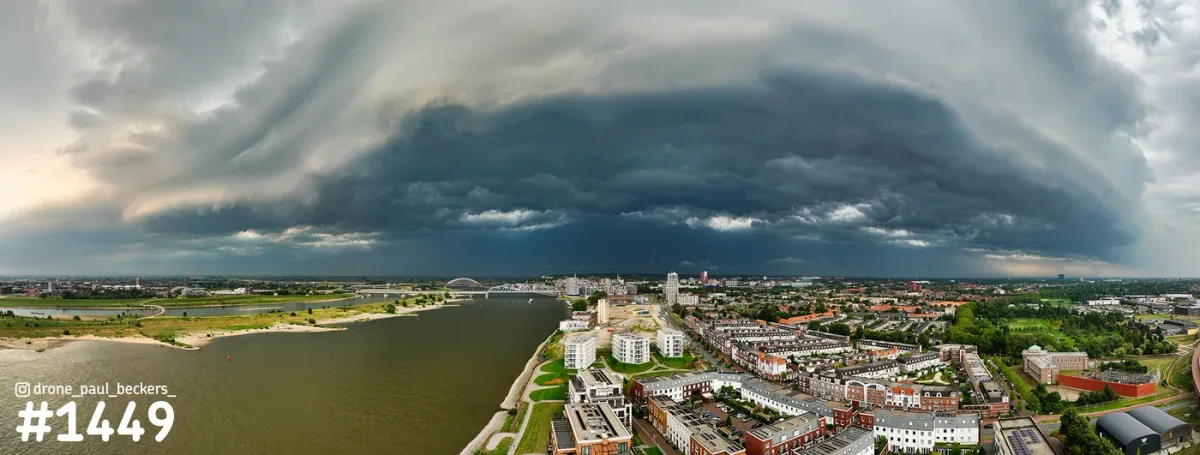 Panorama-luchtfoto van een donkere stormwolk boven de Waal en woonwijken in Nijmegen en Lent, met zandstrand aan de oever