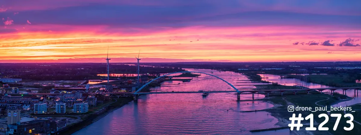 Panorama van de Waal in Nijmegen na zonsondergang, met De Oversteek en het Havenkwartier onder een roze-oranje lucht