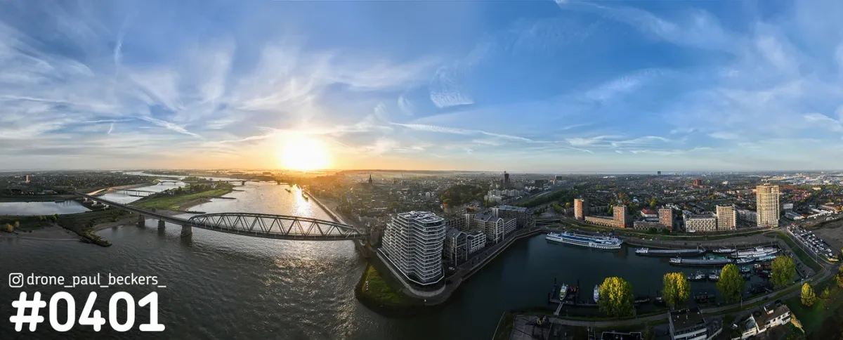 Panoramafoto van de Waal in Nijmegen met laagstaande zon, stalen brug en de Handelskade met een wit woongebouw