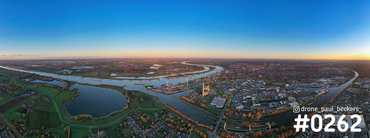 Panoramische luchtfoto van de Waal bij Nijmegen met haven- en industrieterrein, onder een oranje horizon in de herfst