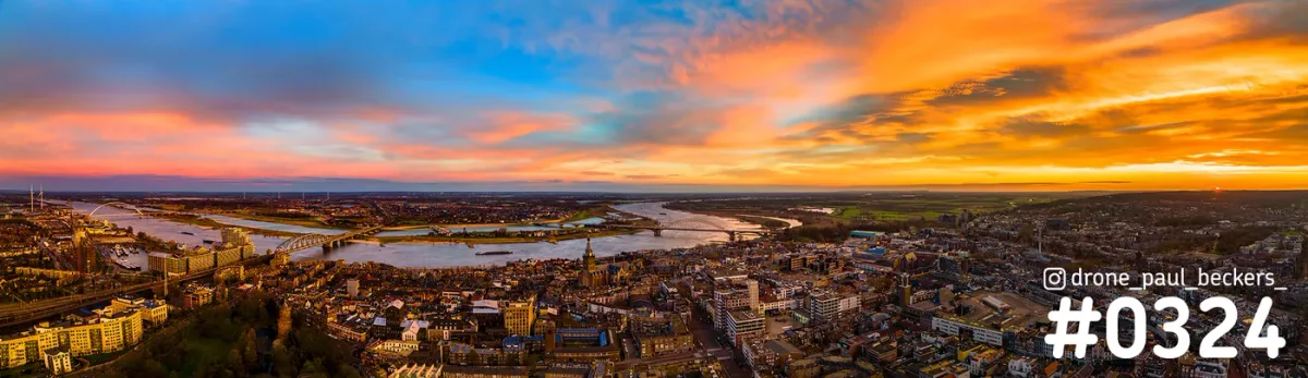 Panorama van Nijmegen met de Waal, de Waalbrug en het Kronenburgerpark onder een gloeiende oranje lucht