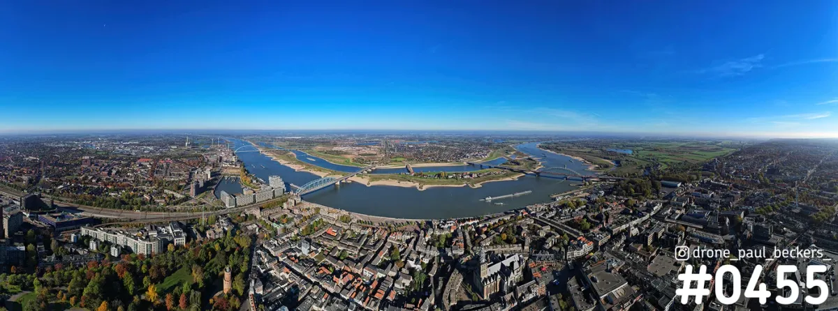 Panorama-luchtfoto van Nijmegen met de Waal, de Waalbrug en het Kronenburgerpark in herfstkleuren onder blauwe lucht