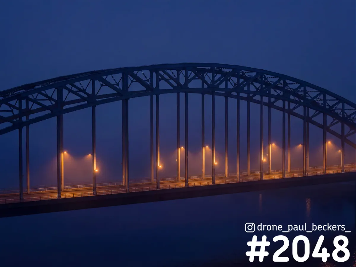 Waalbrug in Nijmegen in de blauwe avondschemering, met oranje straatlantaarns die door de mist boven de Waal gloeien