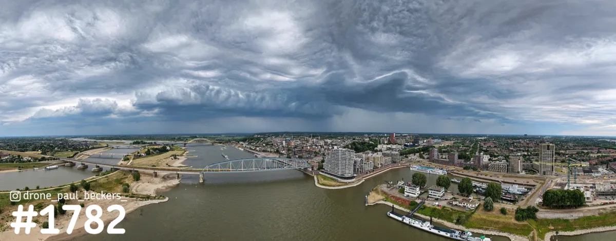 Panoramische luchtfoto van de Waalbrug en het centrum van Nijmegen onder dreigende nimbuswolken boven de Waal