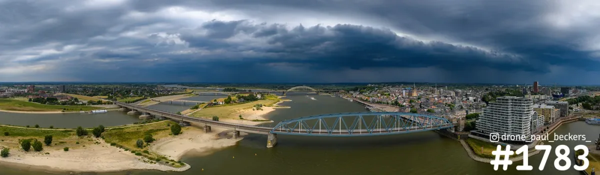 Panorama-luchtfoto van de Waal in Nijmegen met zware, donkere wolken boven de bruggen, Lent en de Handelskade