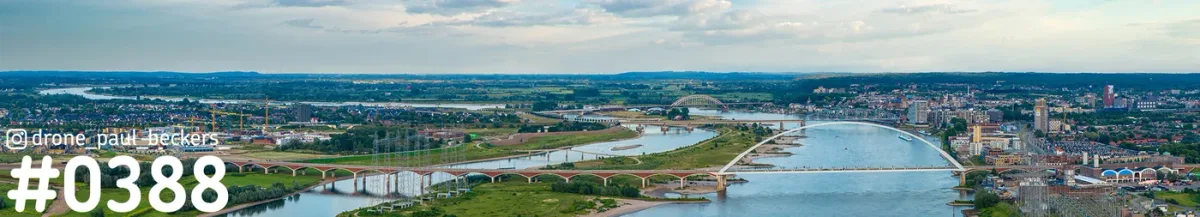 Luchtpanorama van de Waal bij Nijmegen met bruggen, groene uiterwaarden en de stad onder een bewolkte lucht
