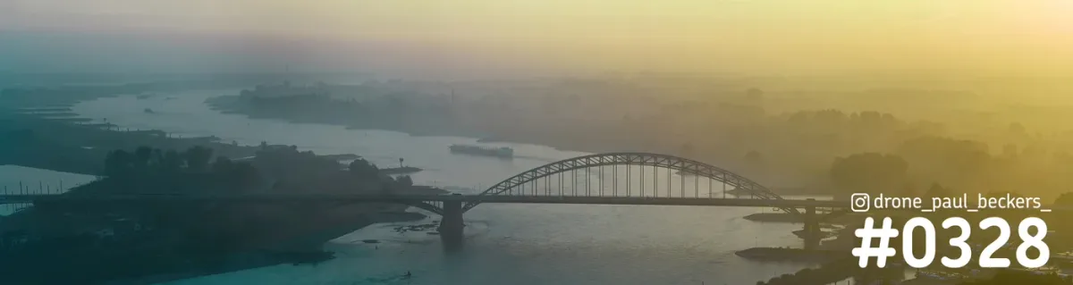 Panoramafoto van de Waalbrug over de Waal in Nijmegen in gouden licht, met mist en nevel boven de rivier