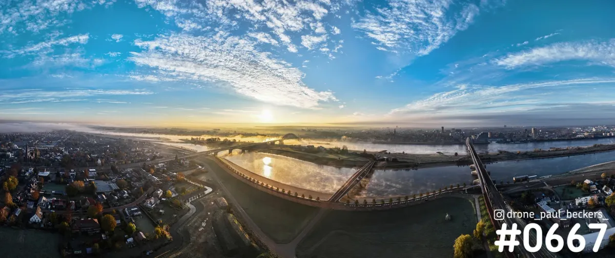 Panoramische luchtfoto van de Waal en de Waalbrug in Nijmegen bij zonsopkomst, met laaghangende mist boven de rivier