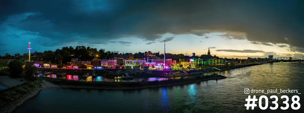 Panorama van de kermis op de Waalkade in Nijmegen in de avondschemering, met donkere wolken boven de Waal