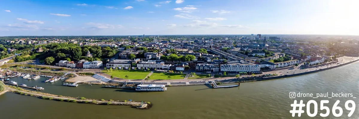 Panorama van de Waalkade in Nijmegen vanaf de Waal, met de Lindenberghaven, een passagiersboot en zonnig stadsgezicht