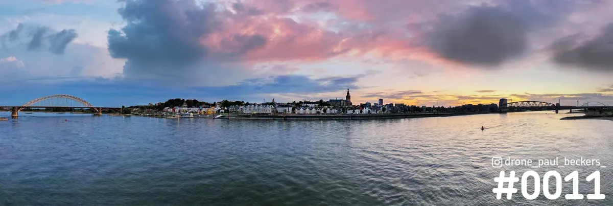 Panorama van de Waalkade en Stevenskerk in Nijmegen aan de Waal bij zonsondergang, met roze wolken en de Waalbrug links